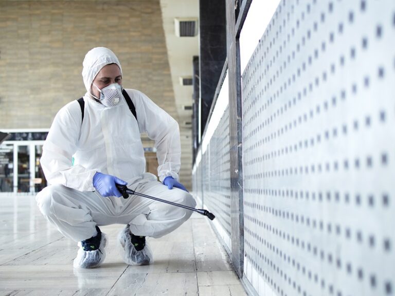 Shot of male person in white chemical protection suit doing disinfection of public areas to stop spreading highly contagious corona virus. Stop coronavirus or COVID-19.
